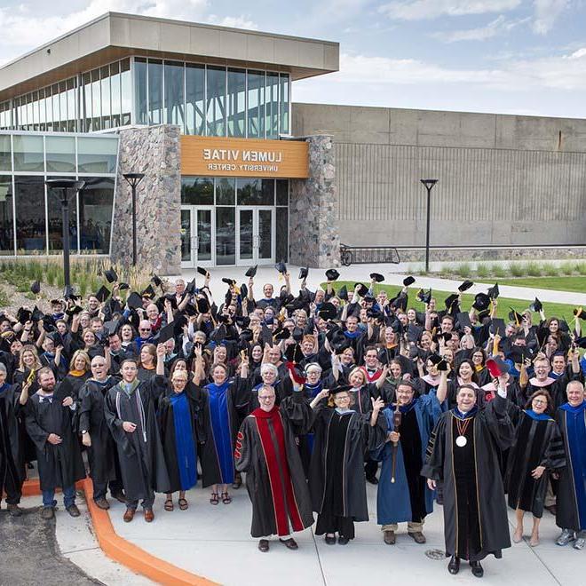 Large group of faculty in their regalia waving outside campus center